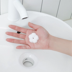White flower-shaped foam on hand from a minimalist facial cleanser foaming bottle dispenser