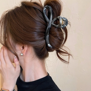 Detail of dark marble pattern acrylic hair claw clip worn on hair with sleek resin finish