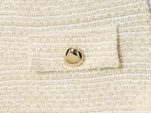 Détail du tissu en tweed avec fils dorés et bouton métallique doré de forme irrégulière