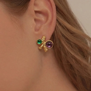 Boucles d'oreilles dorées avec pierres émeraude et violettes sur un mannequin