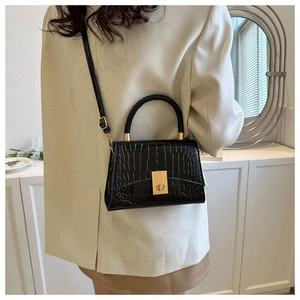 Close-up of black crocodile pattern handbag with woven handle and gold clasp on a model