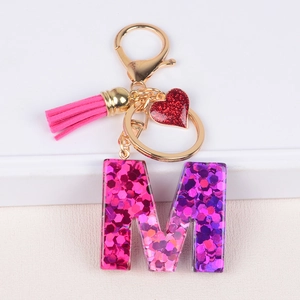 Close-up of pink glitter letter M keychain with heart charm and decorative tassel detail