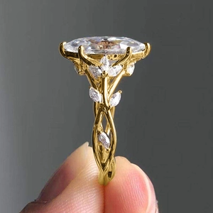 Detail showing marquise-cut crystal ring with golden vine and leaf design on grey background