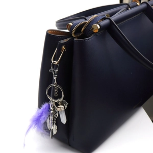 Close-up of purple feather dreamcatcher charm on navy blue leather handbag with gold hardware