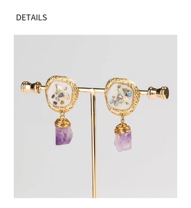 Close-up of golden earrings with crushed sea shells and purple natural crystal stone