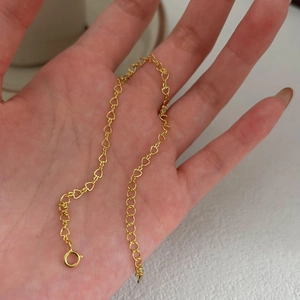 Detailed close-up of golden hollow heart links and spring ring clasp on minimalist bracelet