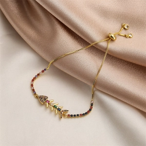 Close-up of golden fishbone bracelet with colorful cubic zirconia on silk background