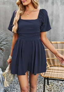 Detailed view of dark blue square neck jumpsuit with waist pleats and clutch bag