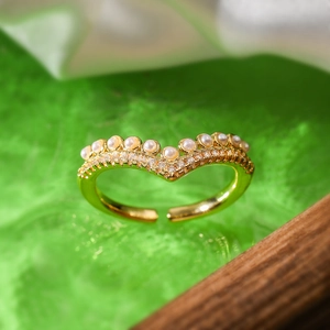 Macro detail of V-shaped gold ring with pearl and zircon inlay on a green textured background
