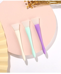 Three colorful silicone mask brushes in white, green, and purple on a decorative stand