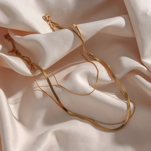 Detail of a 18K gold-plated double-layer snake chain necklace on champagne satin fabric