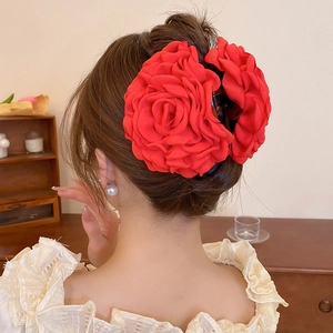 Detail of a large red silk rose hair claw clip worn on hair in a cozy home setting