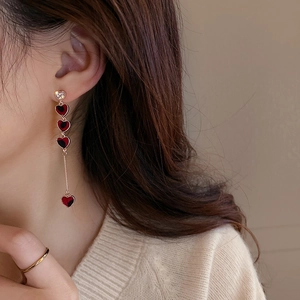 Close-up of asymmetric long tassel heart earrings with rhinestones on a female model