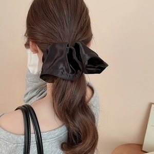 Detail view of a large black satin silk bow scrunchie worn on a female ponytail