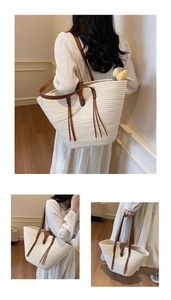 Detail of woven straw tote bag featuring brown leather straps and decorative tassels