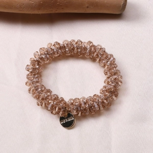 Detail of beaded champagne crystal hair tie with a round gold Morava engraved charm