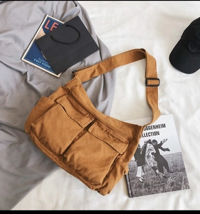Detail of a brown canvas crossbody bag with dual front flap pockets and adjustable strap