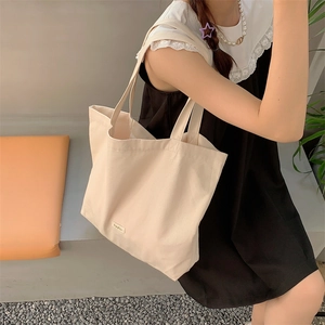 Minimalist off-white canvas tote bag worn by model on shoulder for daily casual look
