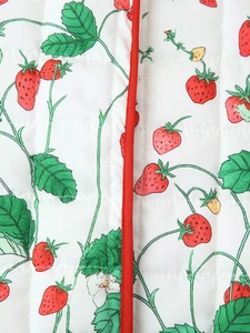 Close-up of white quilted fabric with strawberry print and red piping detail