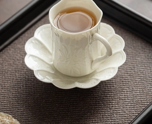 Top view of a cream-white embossed ceramic coffee cup and saucer set on a dark tray