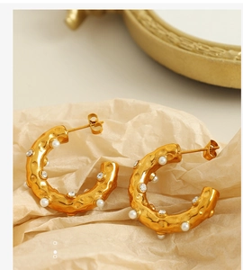 Detailed view of C-shaped gold earrings featuring textured metal, pearls, and crystals