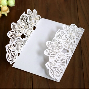 Elegant white laser-cut floral wedding invitation card on dark wood background