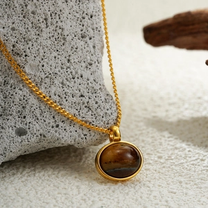 Minimalist 18K gold tiger eye oval pendant necklace displayed on natural stone