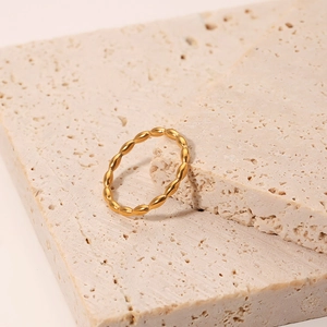 Minimalist gold titanium steel ring with wavy texture on beige travertine display stand