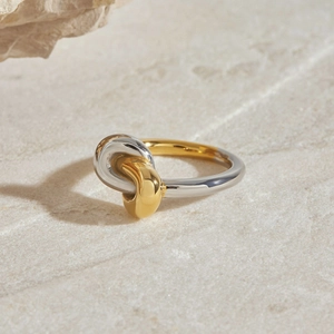 Macro shot of modern two-tone gold and silver knot ring on a natural stone surface