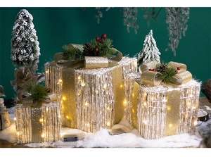 Close-up of three lighted Christmas gift boxes with gold bows and pine needle accents