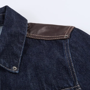 Détail de l'épaule d'une veste en jean avec empiècements en cuir brun et surpiqûres