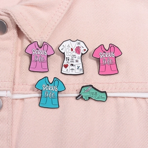 Detail of medical scrubs enamel pins with Scrub Life text and medical tools on pink denim