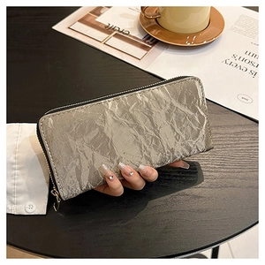 Detail of silver long zip wallet with pleated texture held by hand over black table