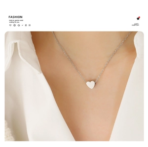 Detail of a minimalist silver heart pendant necklace worn on a white shirt