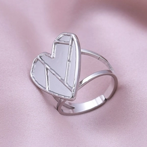 Macro shot of silver heart ring with geometric patterns on pink silk background