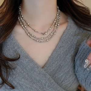 Détail d'un collier à trois couches de perles argentées porté sur un pull gris chic et élégant
