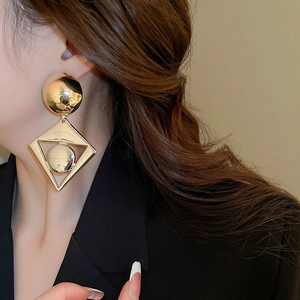 Detail of a large gold geometric rhombus earring featuring a metallic sphere on a model