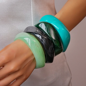 Close-up of four colorful resin bangles in green, black, and blue marble patterns