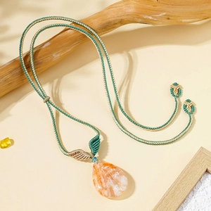 Close-up of a teardrop-shaped orange stone pendant on a woven green and beige cord
