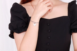 Close-up of a silver heart charm bracelet with Love engraving on a female model