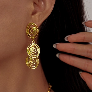 Gros plan de boucles d'oreilles pendantes triple spirale dorées portées sur un mannequin