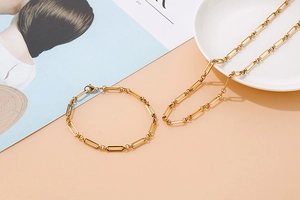 Gros plan sur l'ensemble collier et bracelet à maillons trombone dorés sur un plateau