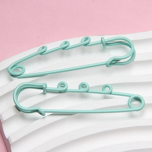 Detail of mint green multi-loop safety pins on a textured white pedestal base