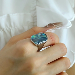Irregular textured ring with iridescent shell inlay shown on hand against white fabric