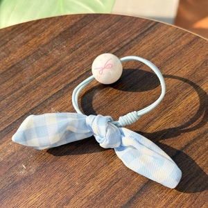 Close-up of light blue checkered bow scrunchie with a pink ribbon bead on a wooden surface