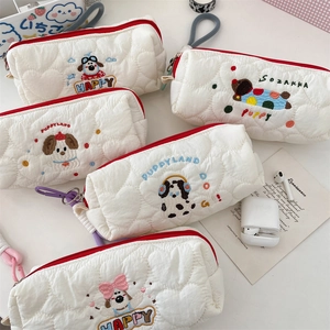 Detailed view of white quilted pencil cases with cute puppy embroidery and red zippers