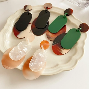 Three pairs of geometric resin hoop earrings with amber and marble patterns on a white plate