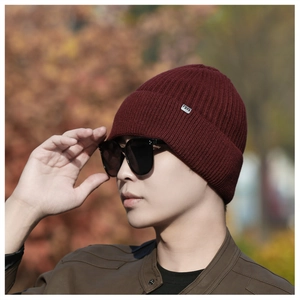 Detail of burgundy ribbed knit beanie for men with metallic brand tag in outdoor setting
