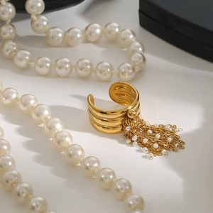 Dettaglio di un anello multistrato dorato con delicati ciondoli a frangia di perle bianche
