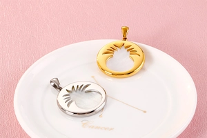 Close-up of gold and silver hollow Cancer zodiac pendants on a white ceramic plate